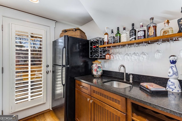 kitchen featuring brown cabinetry, dark stone counters, freestanding refrigerator, open shelves, and a sink