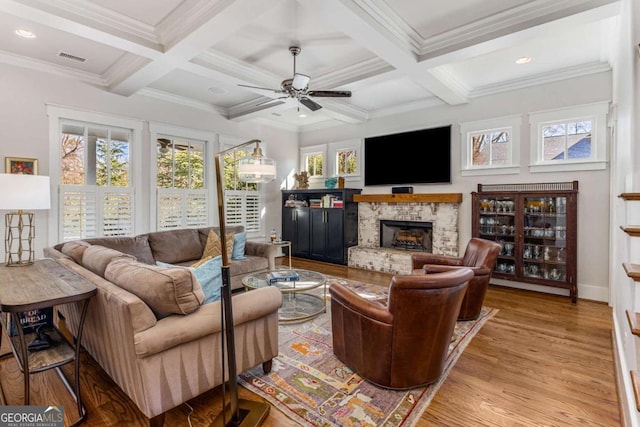 living room featuring a fireplace, coffered ceiling, ornamental molding, light wood finished floors, and beamed ceiling