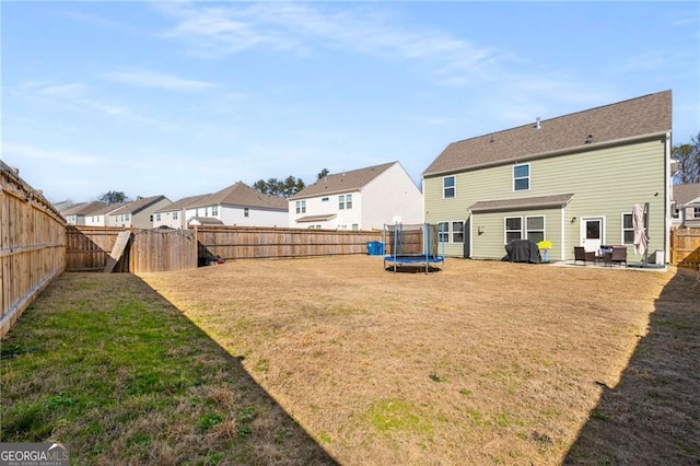 rear view of property featuring a trampoline, a yard, a patio, a residential view, and a fenced backyard