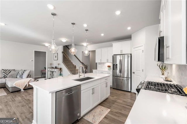 kitchen featuring appliances with stainless steel finishes, open floor plan, a kitchen island with sink, light countertops, and a sink