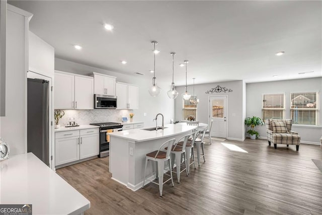 kitchen featuring stainless steel appliances, a sink, a kitchen breakfast bar, decorative backsplash, and an island with sink