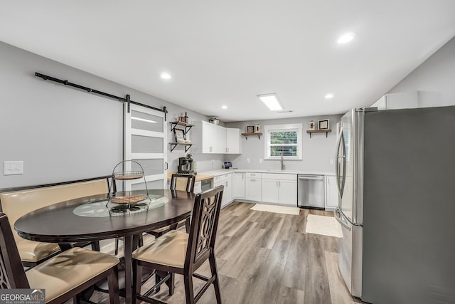 kitchen featuring a barn door, stainless steel appliances, a sink, white cabinets, and open shelves