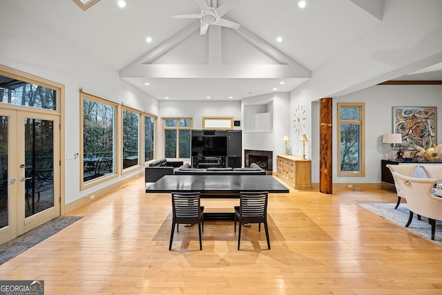 dining space featuring high vaulted ceiling, a fireplace, baseboards, french doors, and light wood-type flooring