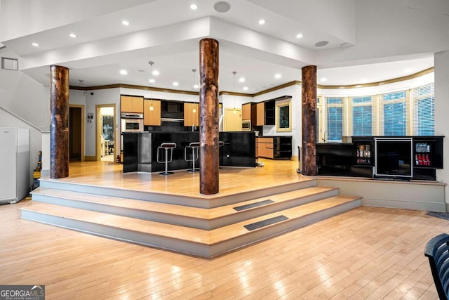 living room with light wood-style floors, recessed lighting, ornamental molding, and ornate columns