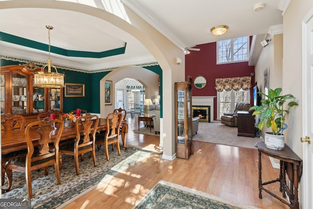 dining room featuring arched walkways, a notable chandelier, a fireplace, wood finished floors, and ornamental molding