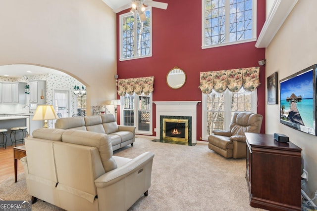 living room featuring arched walkways, light colored carpet, ceiling fan, a high ceiling, and a fireplace