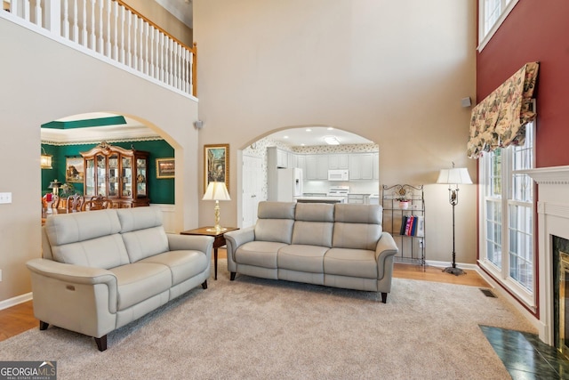 living area featuring a fireplace with flush hearth, arched walkways, visible vents, and a towering ceiling