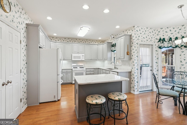 kitchen with white appliances, wallpapered walls, gray cabinets, light wood-type flooring, and a sink