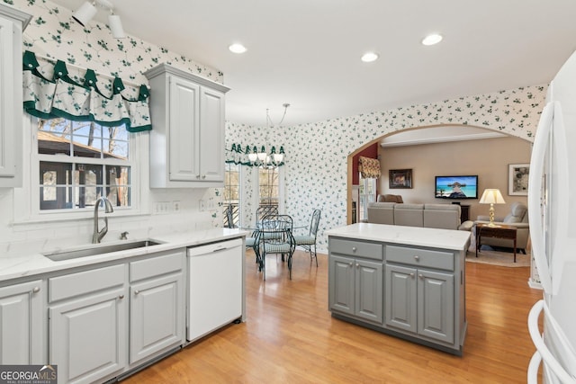 kitchen with white appliances, wallpapered walls, arched walkways, gray cabinets, and a sink