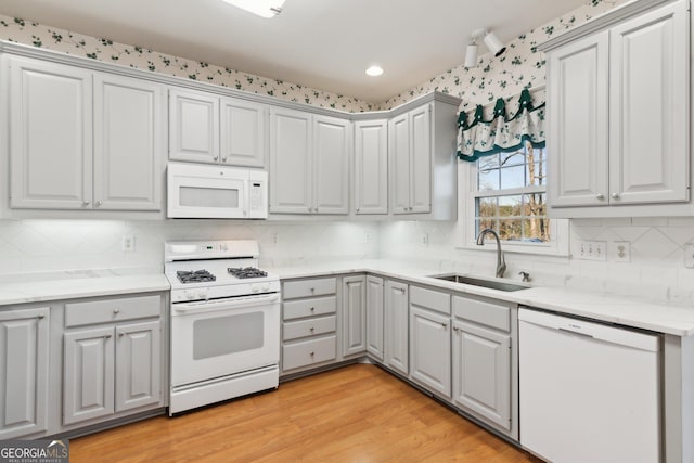 kitchen featuring white appliances, gray cabinets, a sink, and light wood-style flooring