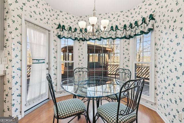 dining room with wallpapered walls, wood finished floors, and an inviting chandelier