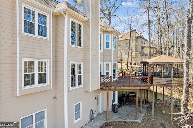 back of property featuring a wooden deck, a chimney, a gazebo, and roof with shingles