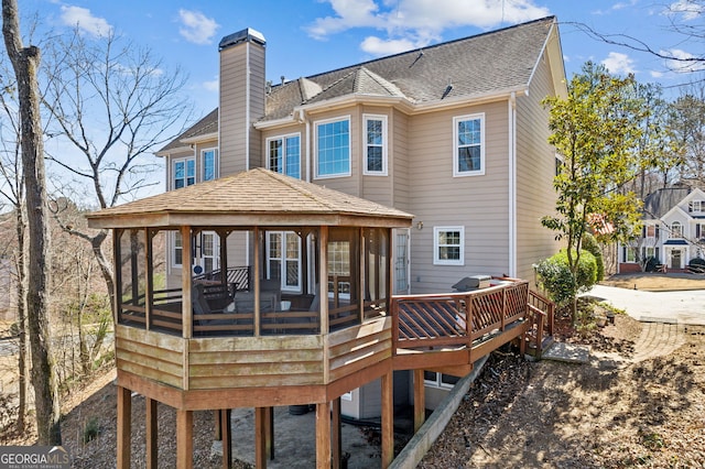 rear view of property featuring a shingled roof, a chimney, and a wooden deck