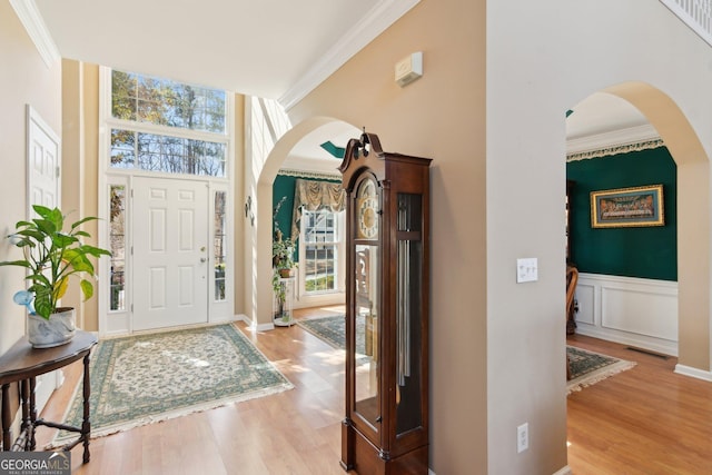 foyer entrance with arched walkways, crown molding, and wood finished floors