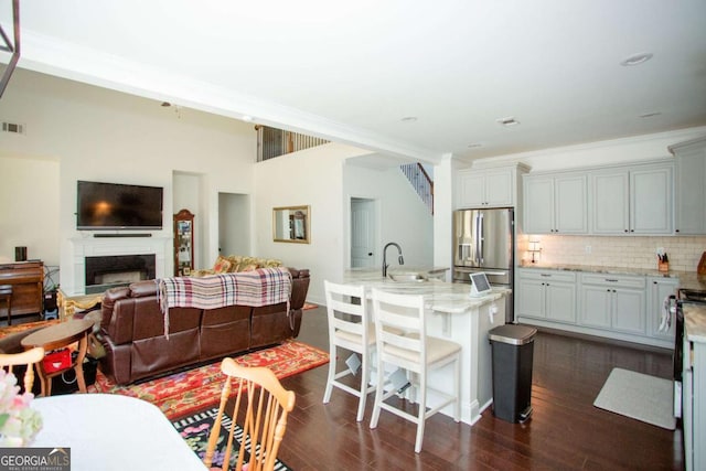 kitchen featuring decorative backsplash, light stone counters, open floor plan, dark wood-type flooring, and stainless steel refrigerator with ice dispenser