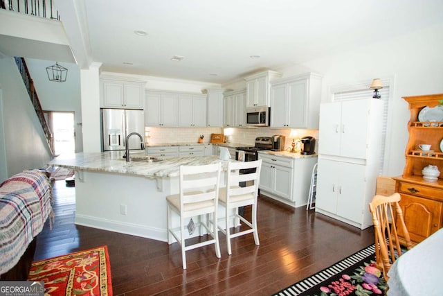 kitchen with light stone counters, decorative backsplash, appliances with stainless steel finishes, dark wood-type flooring, and a sink