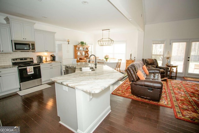 kitchen with appliances with stainless steel finishes, dark wood finished floors, a sink, and tasteful backsplash