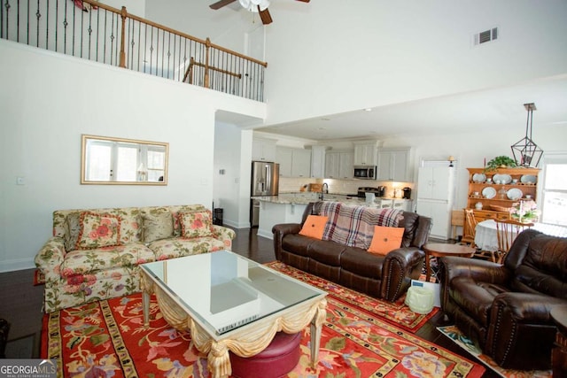 living room with baseboards, visible vents, ceiling fan, wood finished floors, and a high ceiling