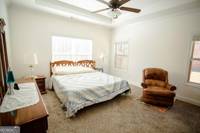 carpeted bedroom featuring ornamental molding, a tray ceiling, baseboards, and a ceiling fan