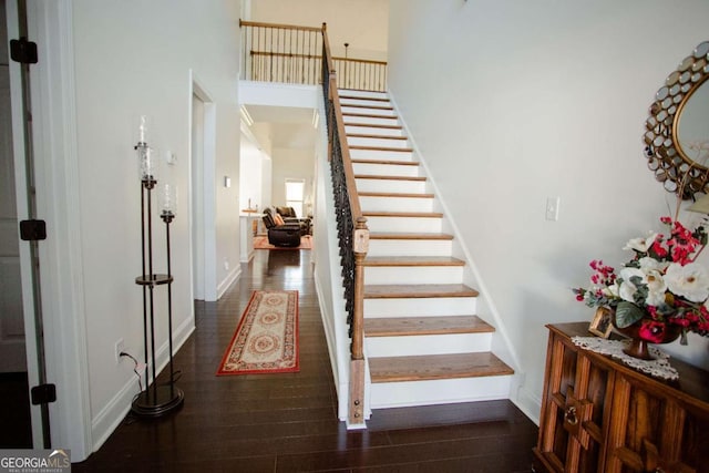 staircase featuring a towering ceiling, baseboards, and wood finished floors