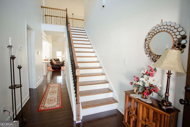 stairs featuring a towering ceiling, baseboards, and wood finished floors