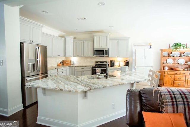 kitchen featuring visible vents, backsplash, appliances with stainless steel finishes, a sink, and a kitchen breakfast bar