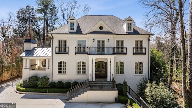 view of front of home with a balcony, metal roof, a standing seam roof, french doors, and brick siding