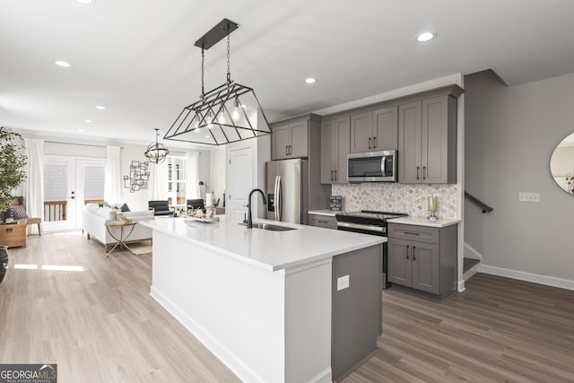 kitchen featuring gray cabinets, light countertops, decorative backsplash, appliances with stainless steel finishes, and a sink