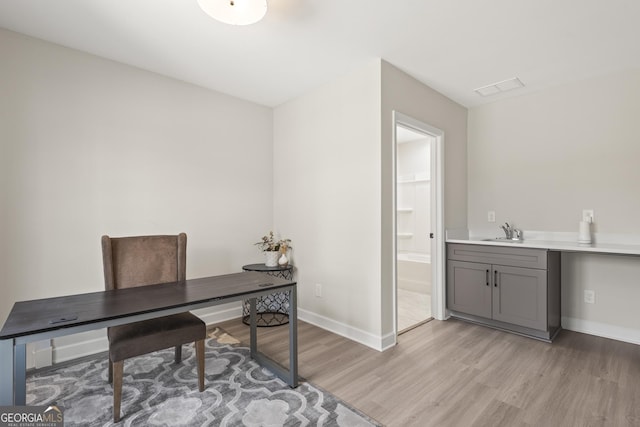 home office featuring visible vents, a sink, light wood-style flooring, and baseboards
