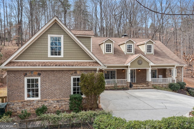 view of front of house featuring covered porch, stone siding, brick siding, and roof with shingles