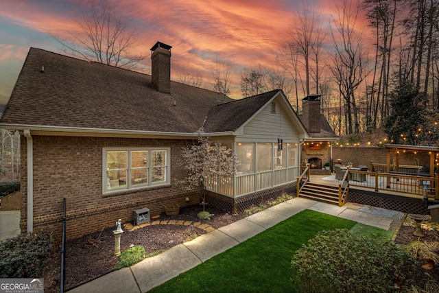 back of property featuring a wooden deck, a shingled roof, a chimney, a yard, and brick siding