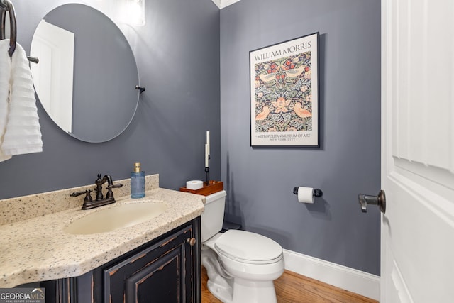 half bathroom featuring toilet, baseboards, wood finished floors, and vanity