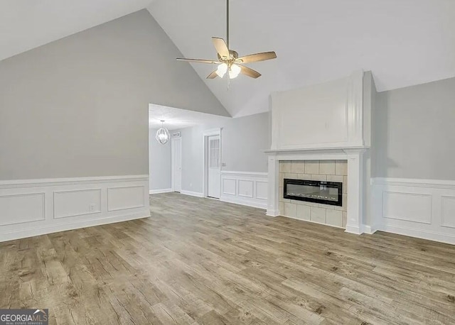 unfurnished living room with a decorative wall, light wood-style flooring, a tiled fireplace, vaulted ceiling, and ceiling fan