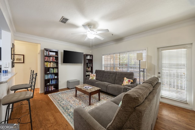 living room with crown molding, visible vents, ceiling fan, and wood finished floors