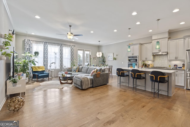 living area featuring baseboards, recessed lighting, ceiling fan, crown molding, and light wood-type flooring