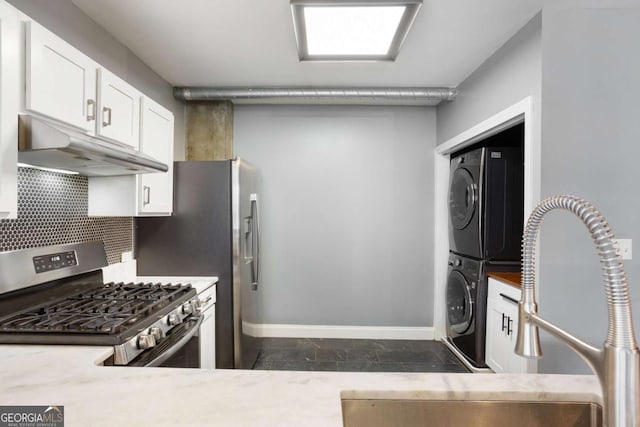 kitchen with stainless steel gas range oven, white cabinets, stacked washer and clothes dryer, under cabinet range hood, and backsplash