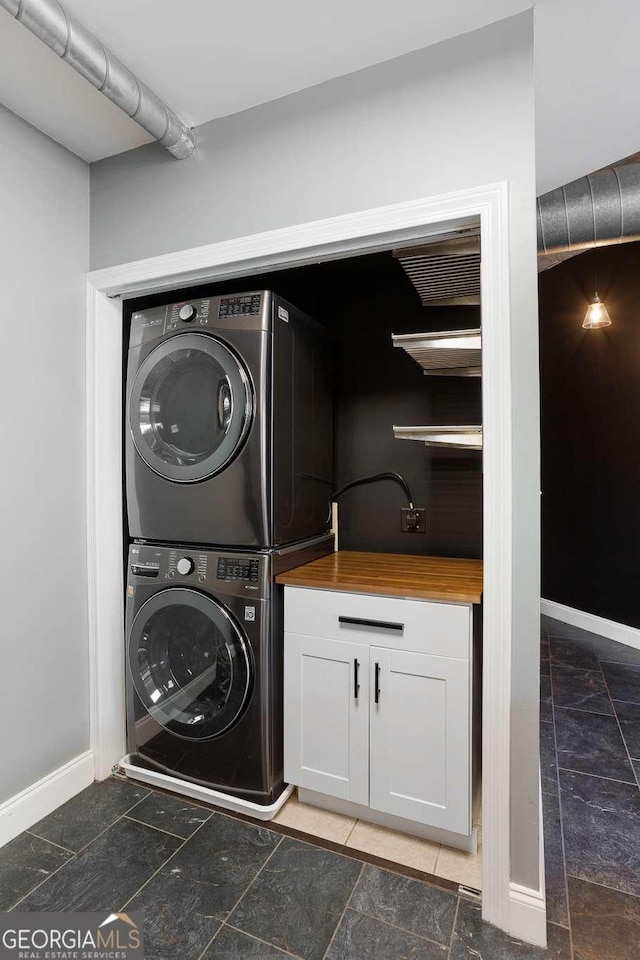 clothes washing area featuring cabinet space, baseboards, and stacked washer / drying machine