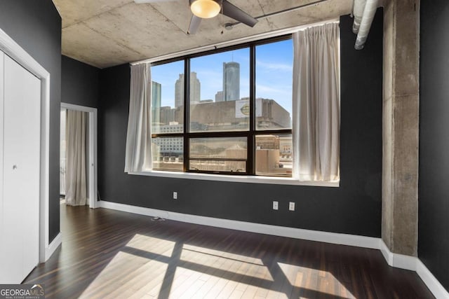 spare room featuring ceiling fan, a view of city, baseboards, and wood finished floors