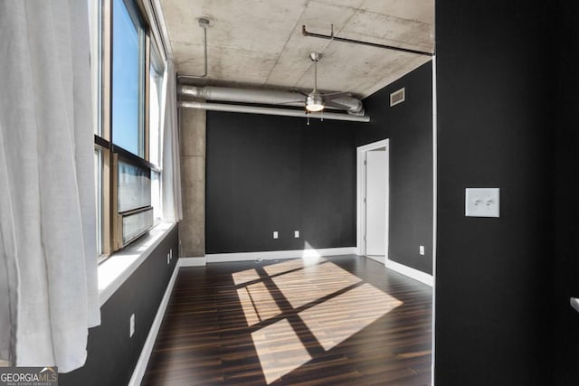 empty room with dark wood-style floors, visible vents, ceiling fan, and baseboards