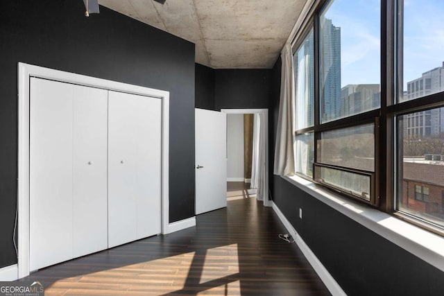 bedroom with a view of city, dark wood-type flooring, a closet, and baseboards