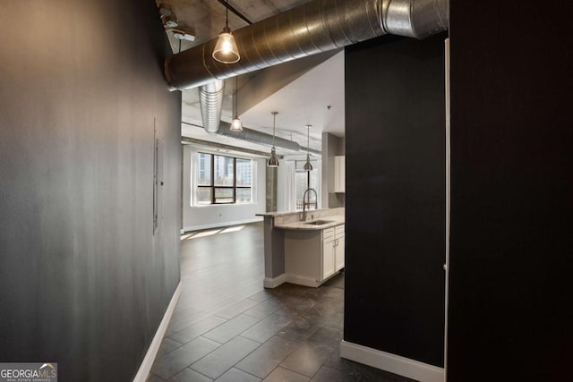 kitchen featuring hanging light fixtures, white cabinetry, a sink, a peninsula, and baseboards