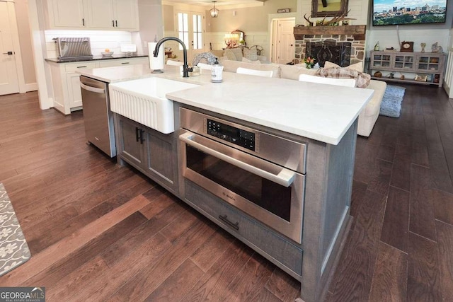 kitchen with a stone fireplace, stainless steel appliances, dark wood-style flooring, a sink, and open floor plan