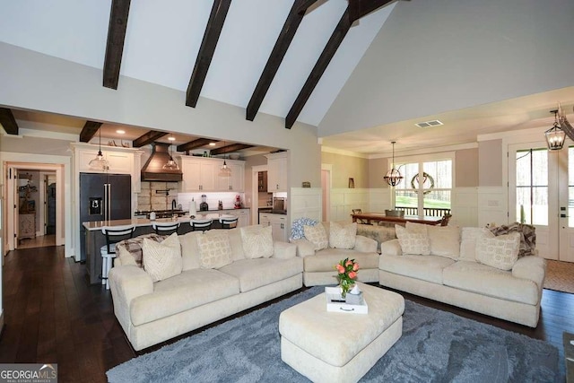 living area with a wainscoted wall, visible vents, beam ceiling, and an inviting chandelier