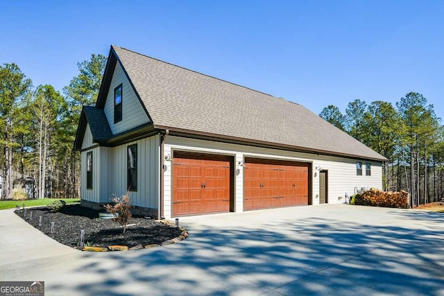 view of side of home with board and batten siding, an attached garage, driveway, and a shingled roof