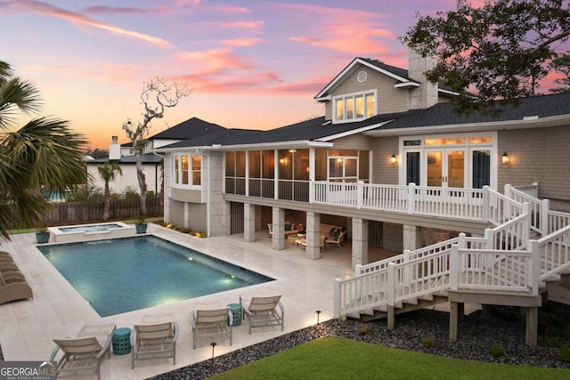 back of property at dusk featuring a patio, a sunroom, a chimney, fence, and french doors