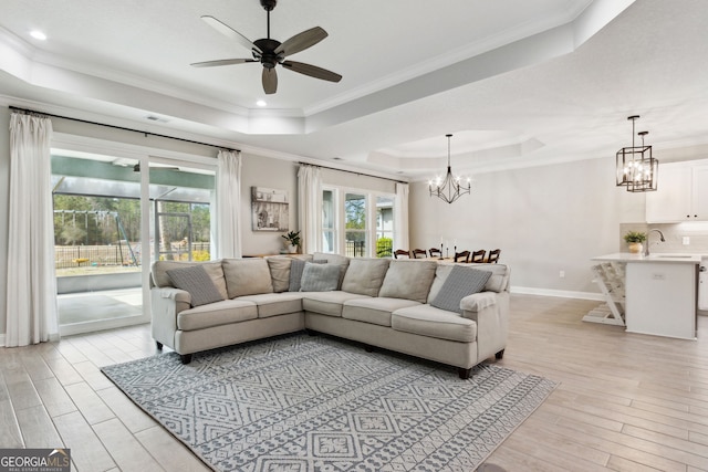 living area featuring baseboards, light wood-type flooring, a raised ceiling, and crown molding