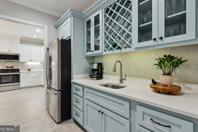 kitchen featuring tasteful backsplash, appliances with stainless steel finishes, light stone counters, ornamental molding, and a sink