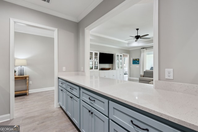 kitchen featuring light stone counters, light wood finished floors, gray cabinets, a raised ceiling, and ornamental molding