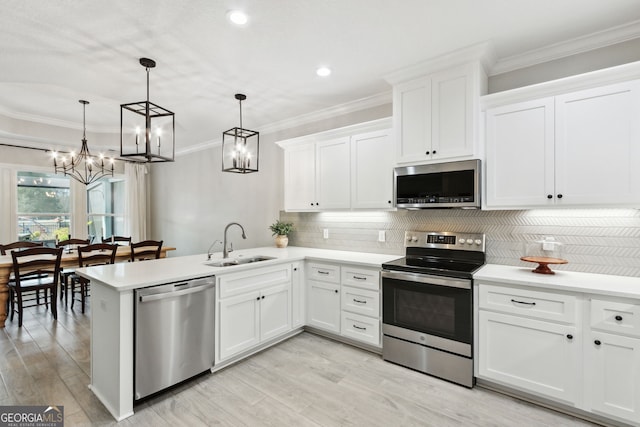 kitchen featuring a peninsula, a sink, light countertops, ornamental molding, and appliances with stainless steel finishes