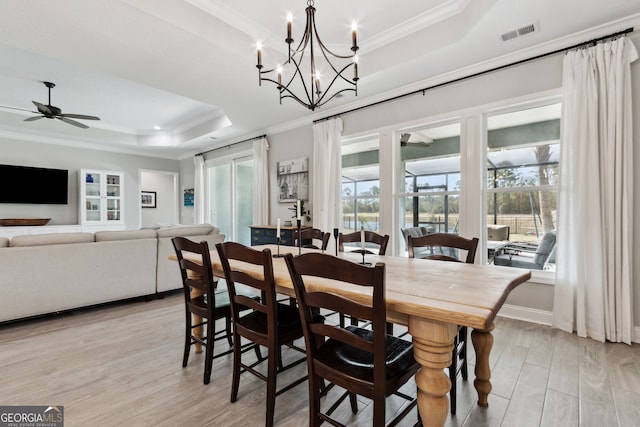 dining room featuring light wood-style floors, a tray ceiling, a healthy amount of sunlight, and visible vents